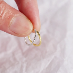 Macro shot of gold and silver twisted hoop earrings held against a white fabric background