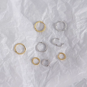 Detailed close-up of textured twist hoop earrings in polished gold and silver finishes