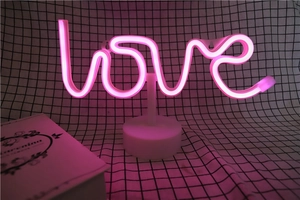 Close-up of pink LED neon Love sign on round white base glowing in a cozy dark setting