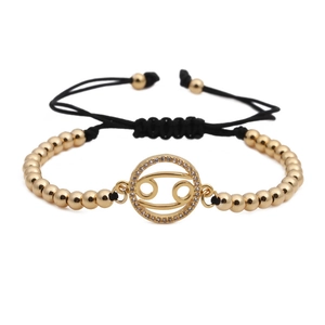 Detail of Cancer zodiac gold-plated charm on black woven adjustable bracelet