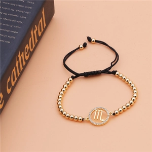 Detailed close-up of a Scorpio zodiac gold beaded adjustable bracelet on a peach background