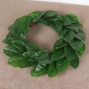 Lush green magnolia leaf spring wreath with brown rattan base on rustic fabric background