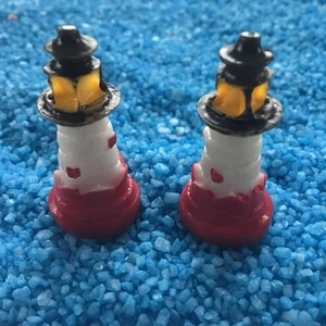 Gros plan de deux phares miniatures en résine sur sable bleu pour micro-paysage DIY décoratif