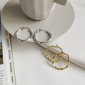 Detailed view of twisted gold and silver hoop earrings on a minimalist lifestyle backdrop