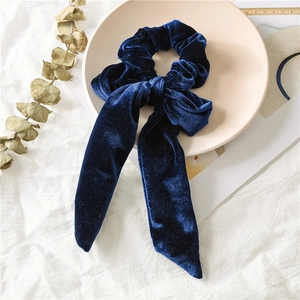 Detail of navy blue velvet scrunchie with large bow and flowing ribbons on a white surface