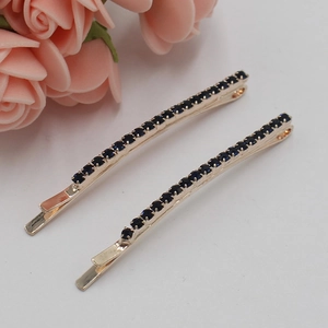 Paire de barrettes dorées en métal avec strass bleu foncé sur fond blanc épuré