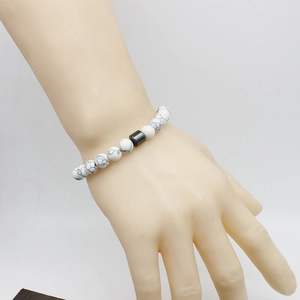 Detailed view of white marble beads bracelet with a metallic cylinder charm on a wrist