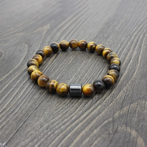 Detail of yellow tiger eye beaded bracelet with hematite cylinder on dark wood surface