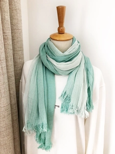 Detail of gradient green to white scarf with crinkle texture and fringe on wooden mannequin