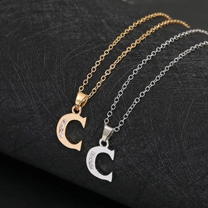 Close-up of gold and silver letter C pendants with inlaid crystals on a black background