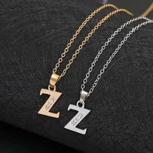 Detail shot of gold and silver Z-letter necklaces with crystal inlay on black surface