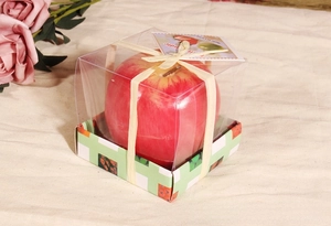 Detalle de vela con forma de manzana roja en caja de regalo con cinta de rafia