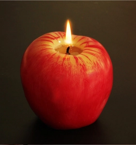 Primer plano de una vela roja en forma de manzana encendida con textura de fruta realista