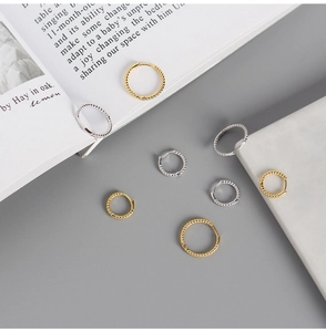 Close-up of twisted rope hoop earrings in gold and silver finish on minimalist background
