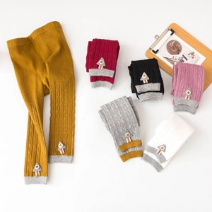 Detailed close-up of colorful knitted baby leggings with cute tree patch and cable texture