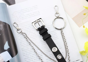 Detail of a black punk belt featuring silver metal chains and eyelets on a book background