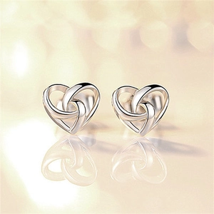 Macro view of silver heart knot stud earrings on a reflective surface with bokeh background