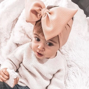 Detailed close-up of a peach pink waffle knit baby headband with a large bow on an infant