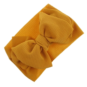 Detailed macro view of a mustard yellow textured fabric baby headband with a bow