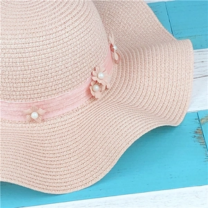 Pink straw sun hat with floral pearl accents and wavy brim for summer beach travel