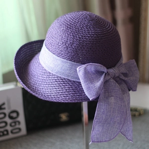 Elegant purple straw sun hat with large bow decoration on a metal display stand
