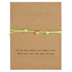 Detail of light green braided wish bracelet with a golden heart charm on a kraft card