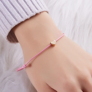 Adjustable pink woven rope bracelet with gold heart pendant worn on woman's wrist