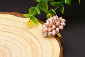 Macro d'une bague fleur artisanale avec perles roses et fil doré sur un support en bois