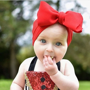 Close-up of a red bow headband on a baby with knitted texture and sequin outfit