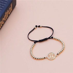 Macro view of Gemini zodiac charm bracelet with gold beads and black braided rope