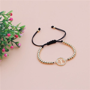 Detail of Aries zodiac charm on a gold copper bead and black braided adjustable bracelet