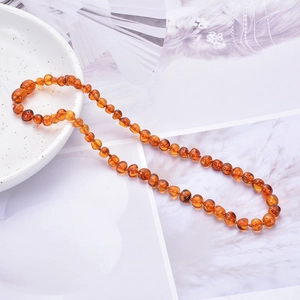 Handmade Baltic amber beaded necklace for babies displayed on a white ceramic plate