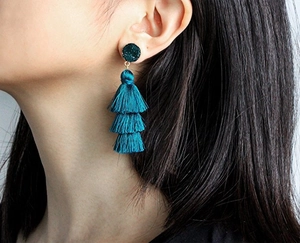 Detail of dark teal three-layer tassel earrings worn by a model for a side-view close-up