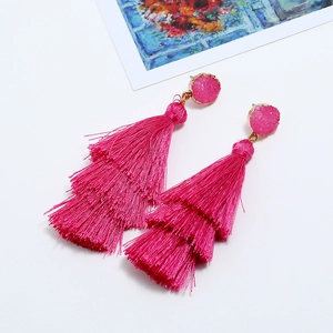 Close-up of pink three-tier tassel earrings with sparkling studs and gold details