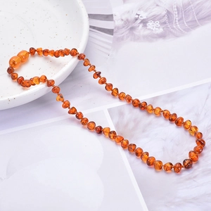 Natural Baltic amber baby necklace with small polished beads on a white ceramic plate