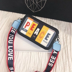 Détail du sac carré noir à bandoulière large imprimée avec logo PEACE et texte mode