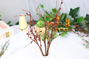 Close-up of artificial berry stem with red and green beads in a white ceramic vase
