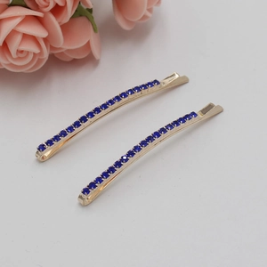 Gros plan de deux barrettes dorées serties de strass bleus sur fond blanc