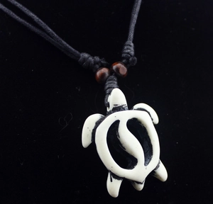 Macro detail of white faux bone sea turtle pendant with black woven cord and beads