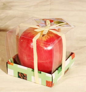 Detalle de vela con forma de manzana roja en caja de regalo con lazo de color crema
