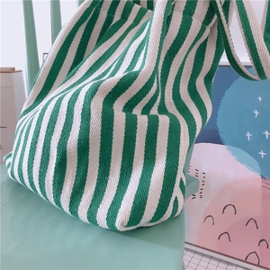 Detailed view of a green and white striped canvas tote bag on a rustic chair
