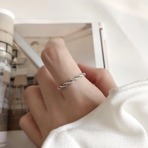 Detail of a thin twisted silver rope ring on finger with elegant aesthetic background