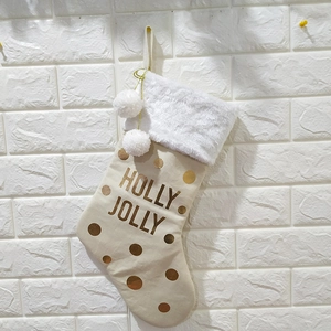 Détail d'une chaussette de Noël beige avec pois dorés et pompons blancs sur mur en pierre
