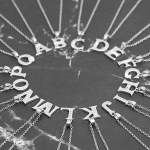 Silver copper alphabet necklace with cubic zirconia pendants on dark marble background