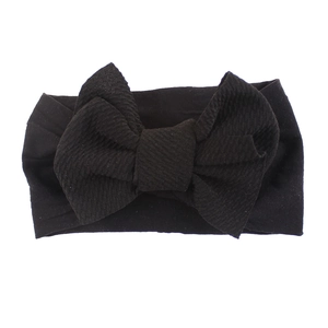 Close-up of a soft black nylon baby headband featuring a large ribbed fabric bow detail