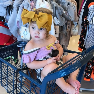 Toddler girl wearing bright yellow bow headband with purple ruffled baby romper