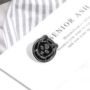 Macro detail of a punk style black enamel cat head brooch on a white art card