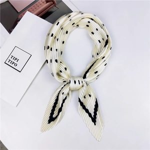 Détail d'un foulard plissé en soie beige à pois noirs et rayures noué avec élégance