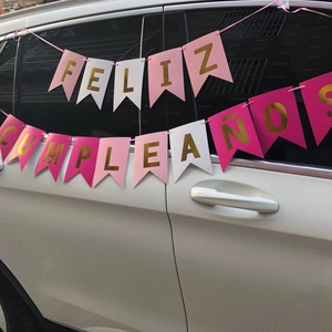 Pink and white Happy Birthday banner with gold letters hung on a white car outdoors
