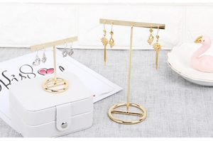 Set of two gold T-bar earring display stands on a stylish marble tabletop with props